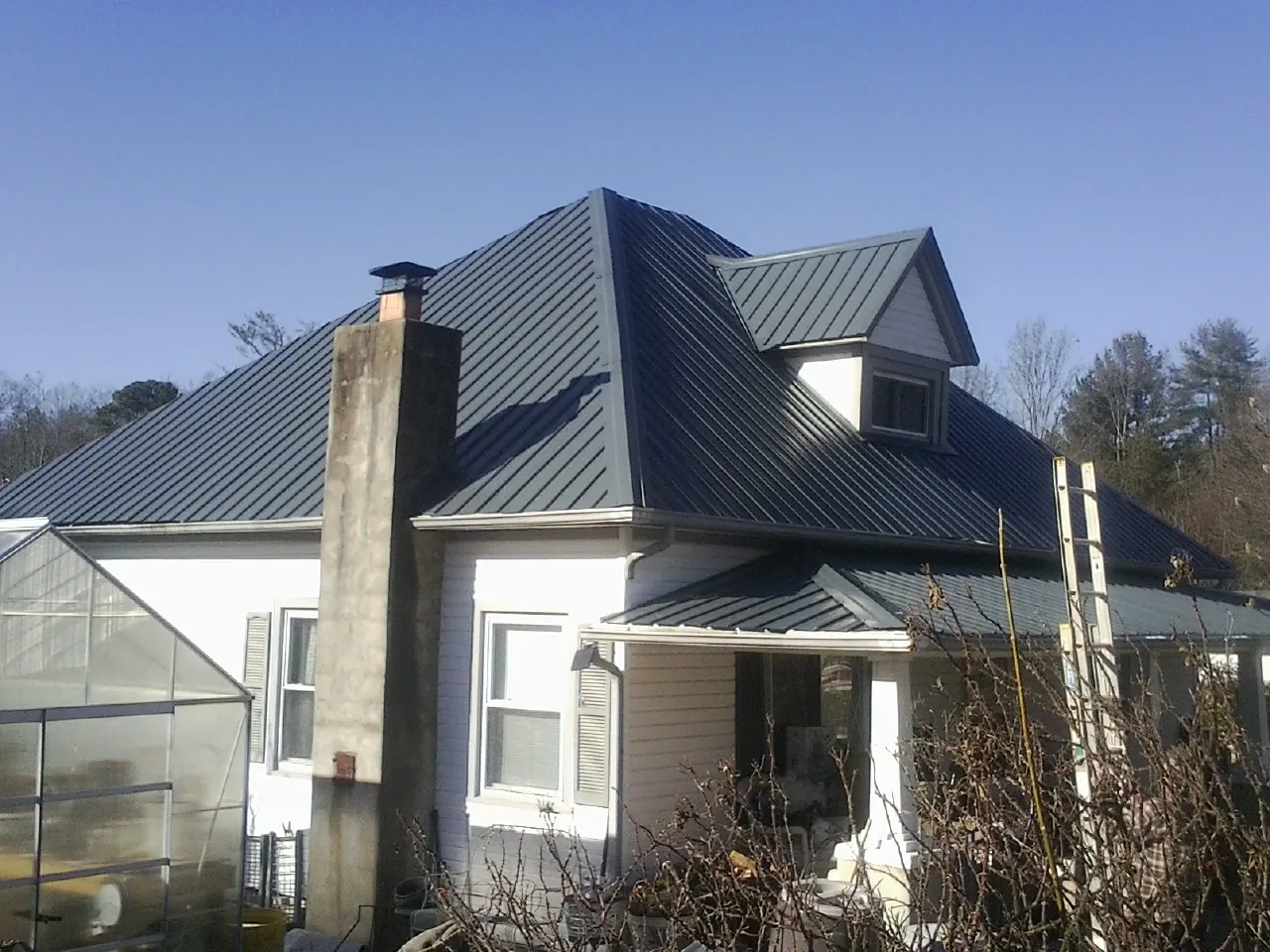 Dark blue standing seam metal roof on a white farmhouse with dormer — Slate & Tile Roof Repair by Roofing Brothers in Okauchee
