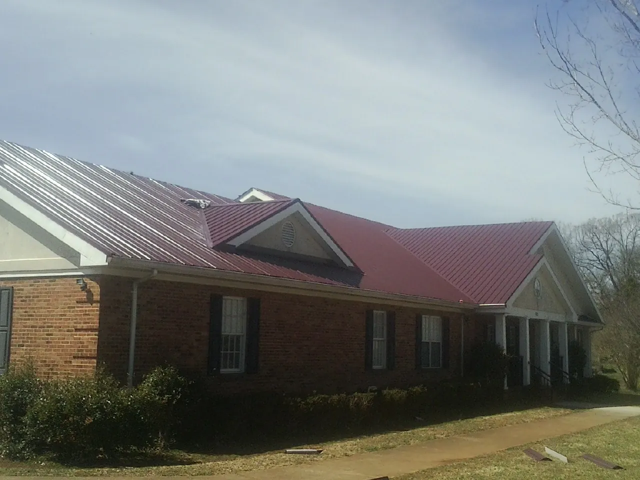 Red metal roof with gabled entries on a long brick building, from a Hail Damage Roof Repair job in Okauchee