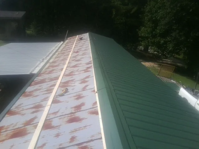 Old rusted panels beside newly installed green metal roofing — Wind Damage Roof Repair by Roofing Brothers in Okauchee