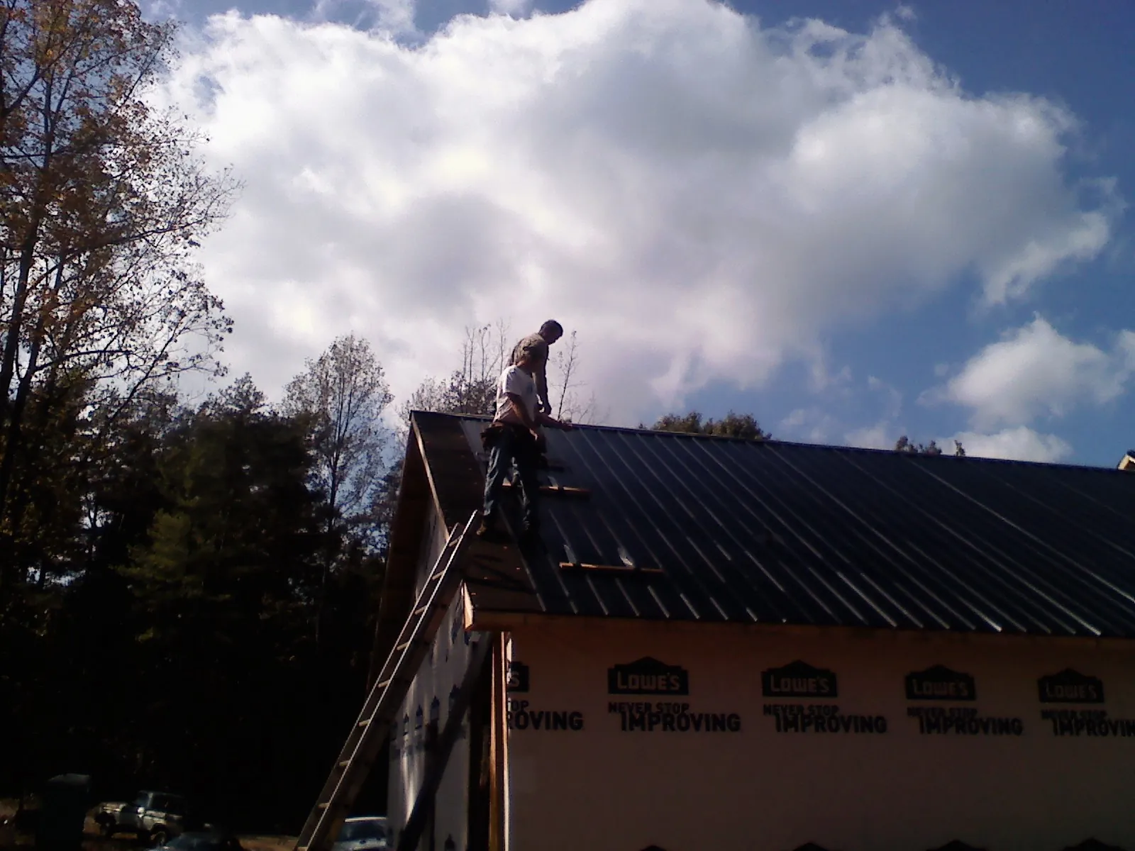 Roofer fastening dark metal panels high against a cloudy sky, from a Roof Inspection job in Okauchee